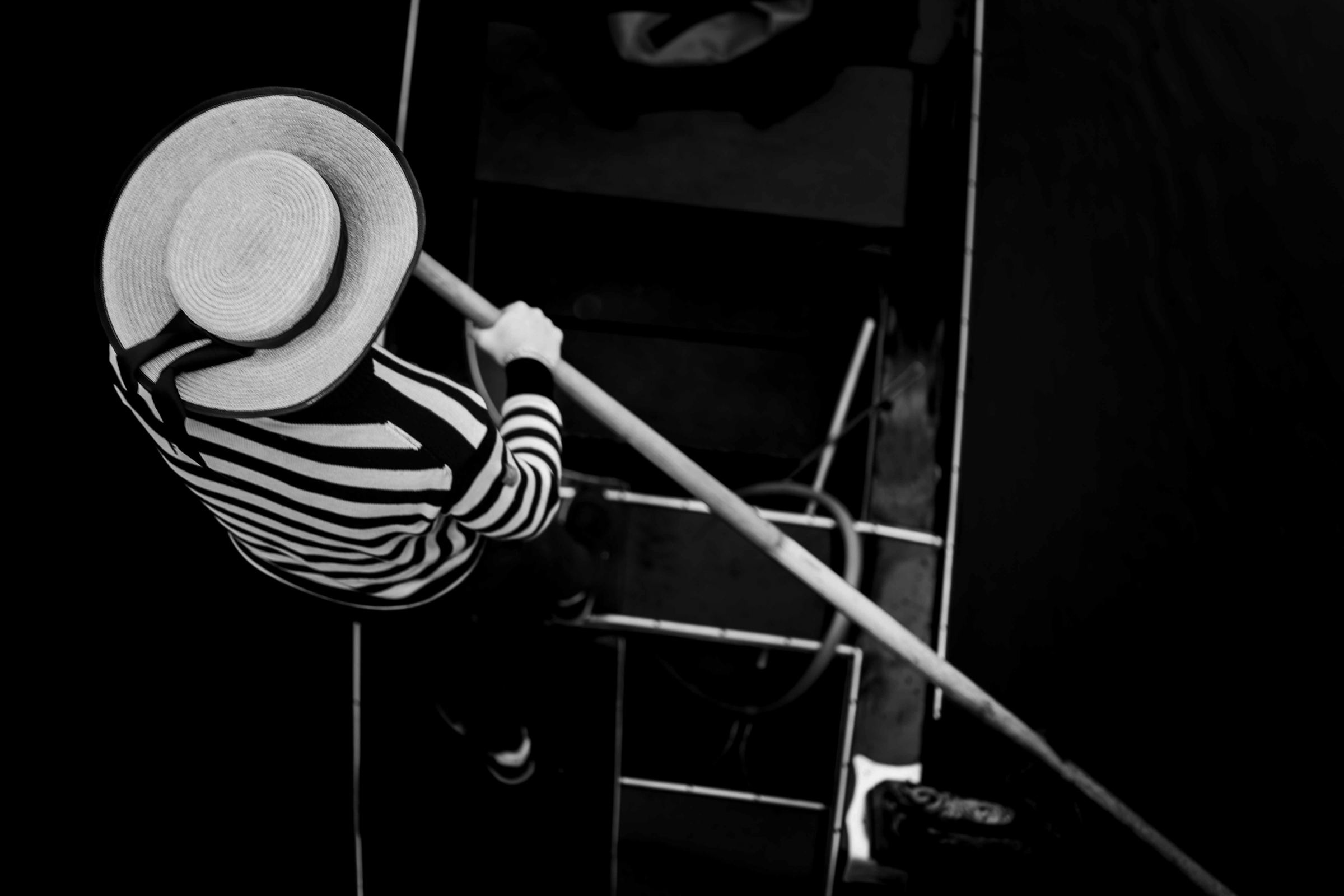 Black-and-white photograph: A gondolier in a striped shirt and straw hat, seen from above