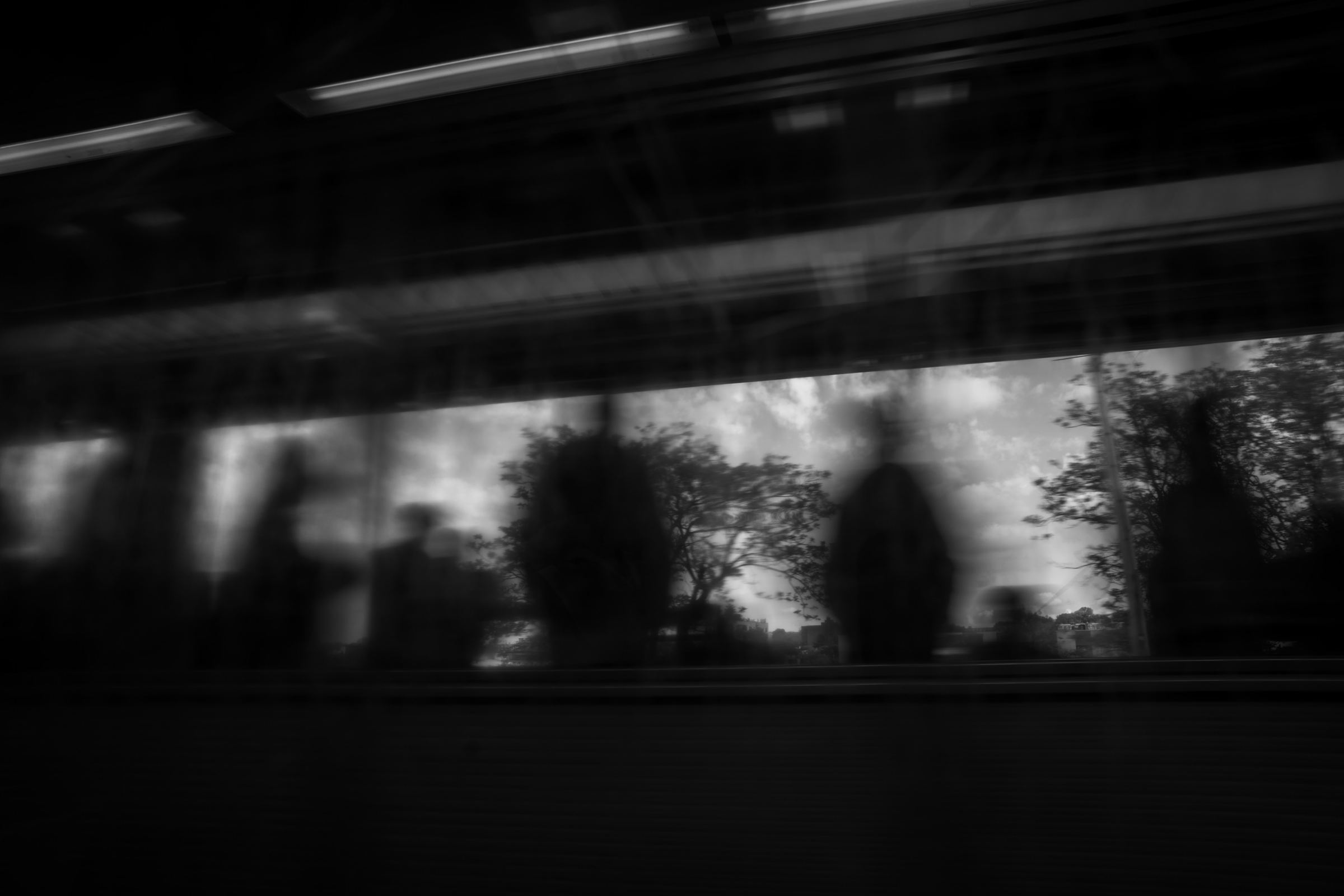 Black-and-white photograph: Blurred figures reflected in a moving train window